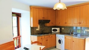 A compact kitchen with wooden cabinets, a microwave, a washing machine, and a dining area with a table and chairs.