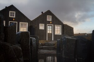Un edificio rústico de madera con entrada de piedra y un pequeño estanque al frente.