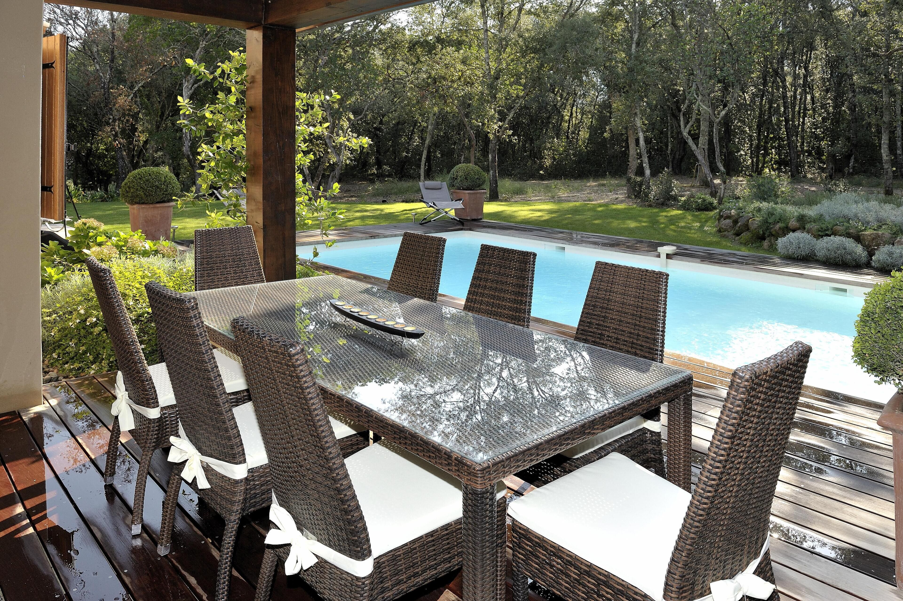 An outdoor dining area with wicker furniture and a view of a swimming pool.