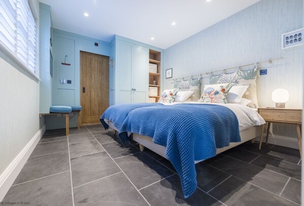 A bedroom with a bed, a nightstand, a wardrobe, and a window with blinds. - Wella 5* Gold Rated Luxury Cottage (St Ives)