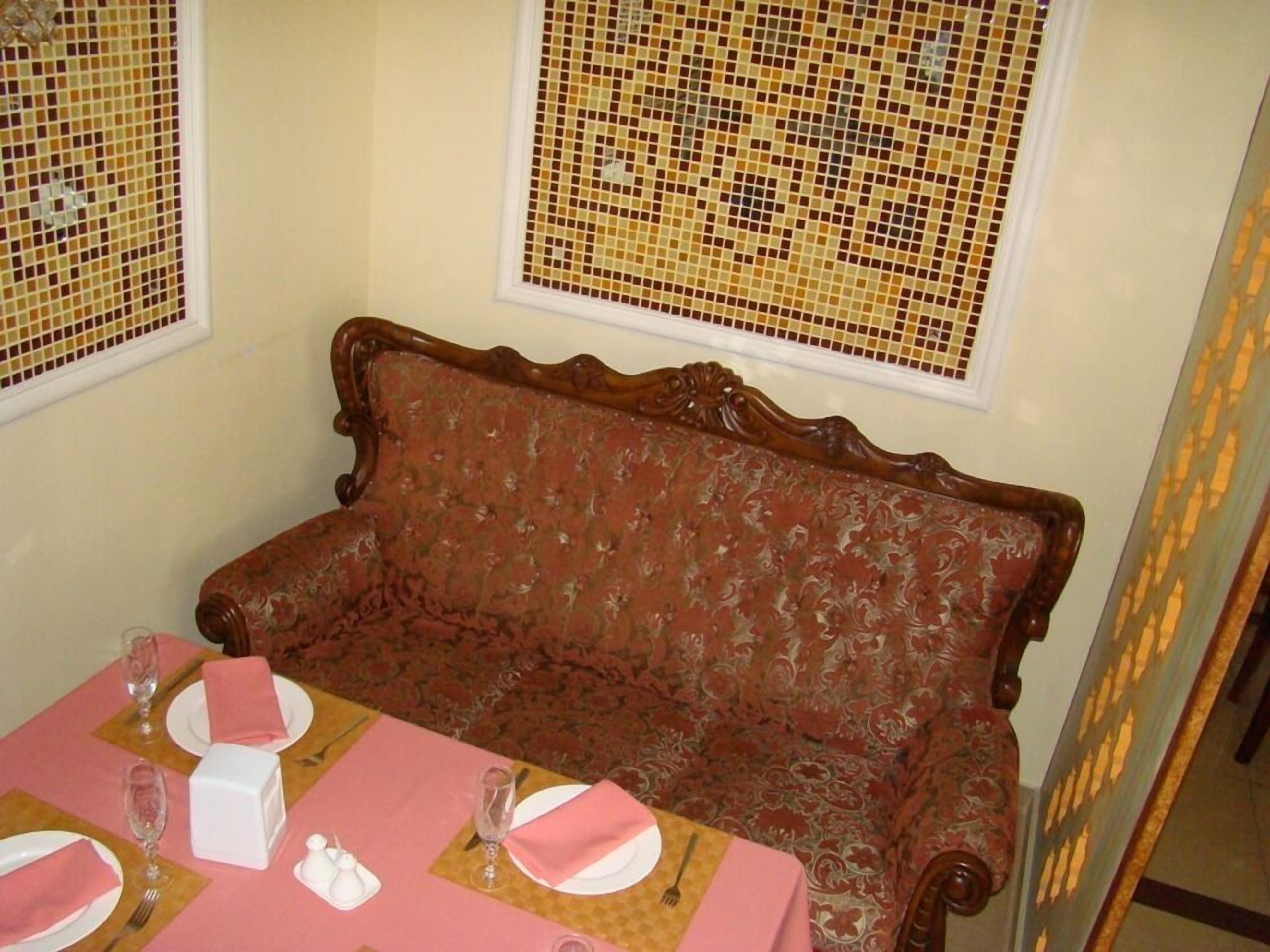 A dining area with a wooden bench, pink tablecloth, and a window with a mosaic pattern.