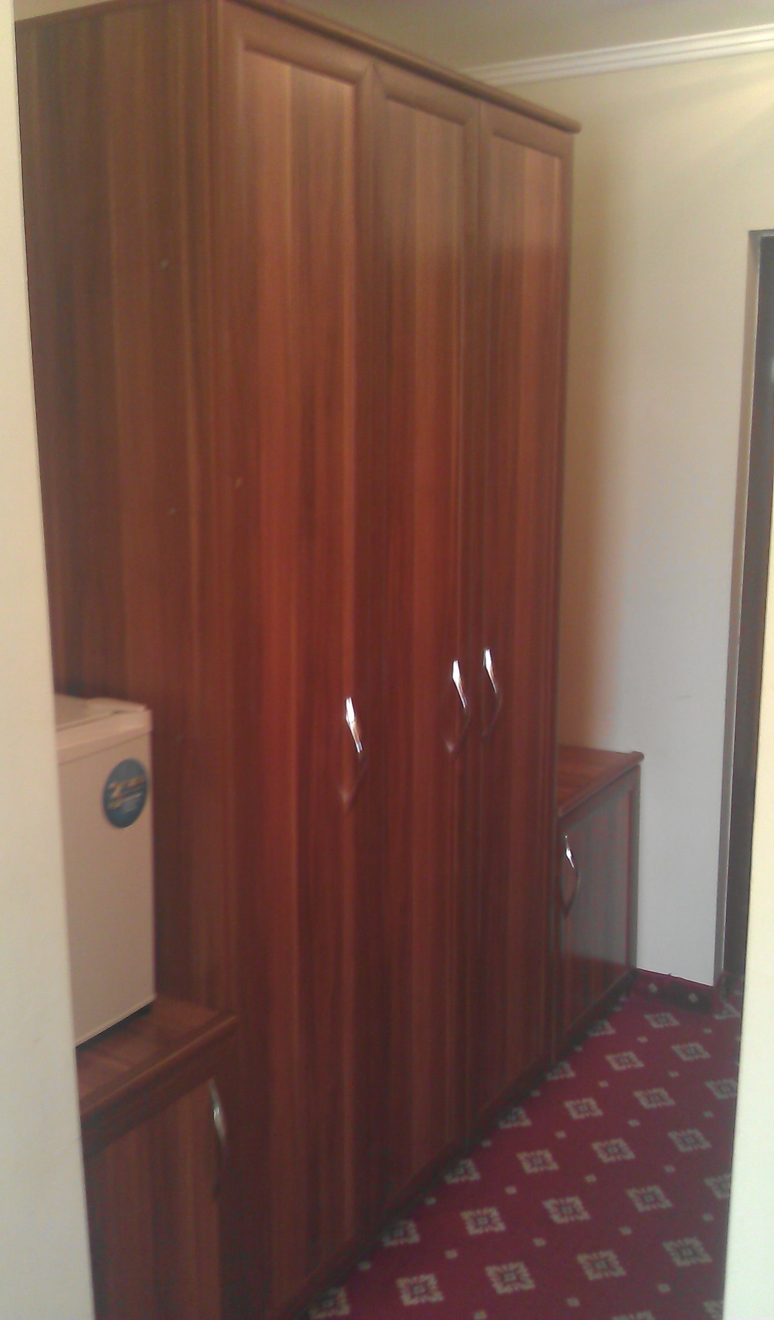 Una habitación con un armario grande de madera, un mueble pequeño y una alfombra estampada.