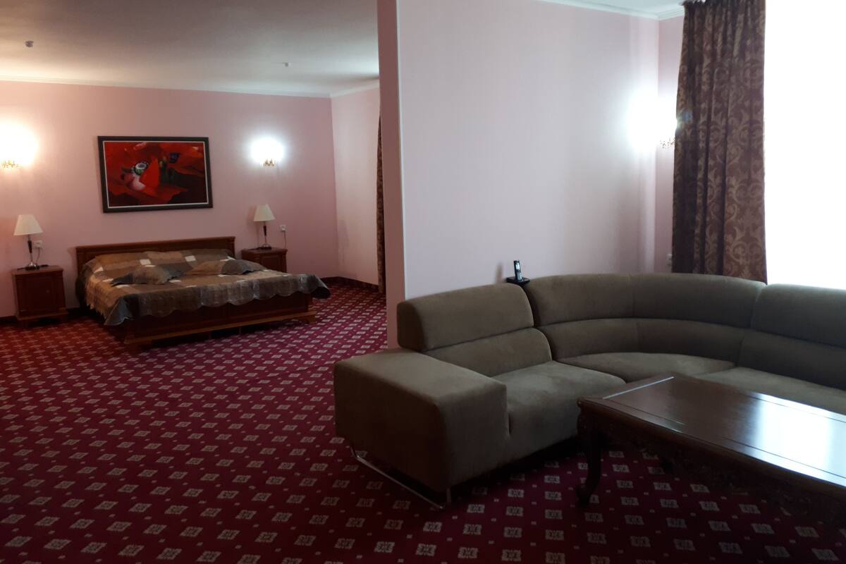 A hotel room with a bed, a sofa, a patterned carpet, and a painting on the wall.