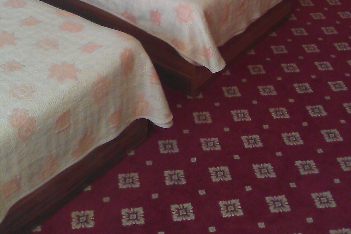 A hotel room with two single beds, a nightstand, a mirror, and a patterned carpet.
