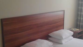 A hotel room with a wooden headboard, a neatly made bed with white linens, and a small bedside table with a lamp.