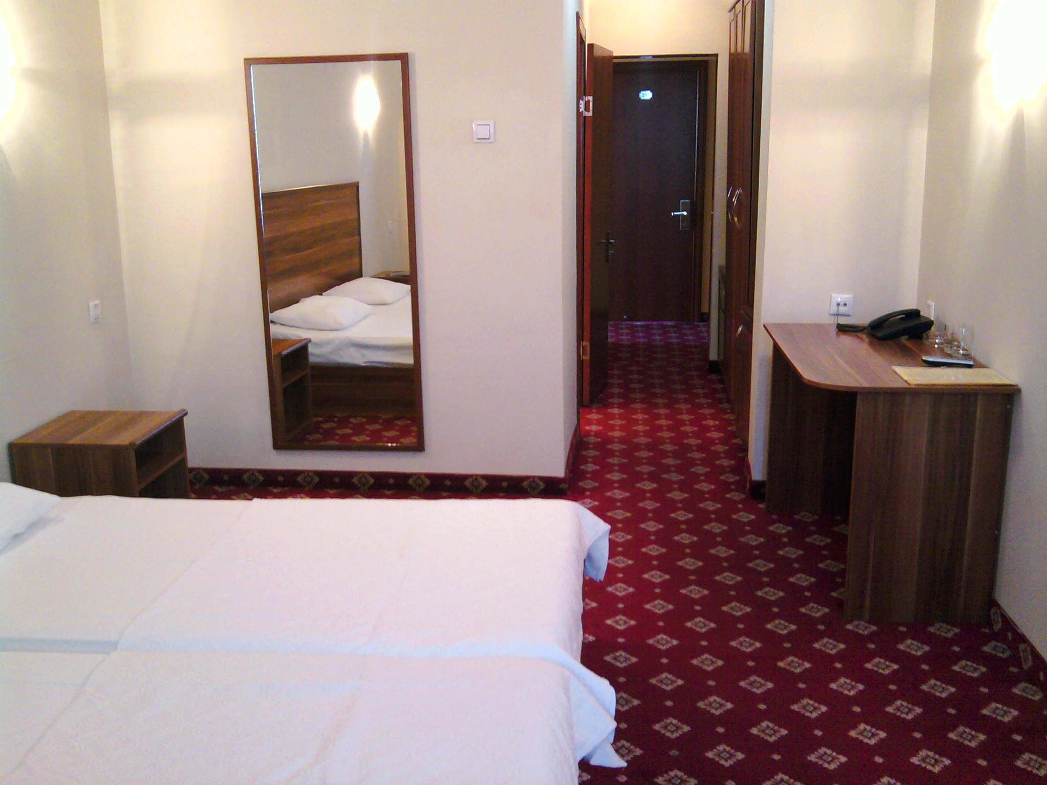A hotel room with a large bed, a desk with a telephone, and a mirror on the wall.