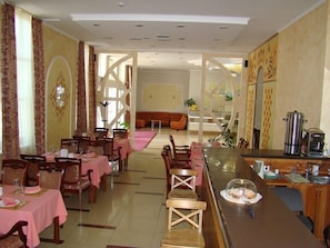A dining area with tables set for two, a bar area with coffee machines, and a seating area with sofas. - Silk Way Hotel (Aktau)