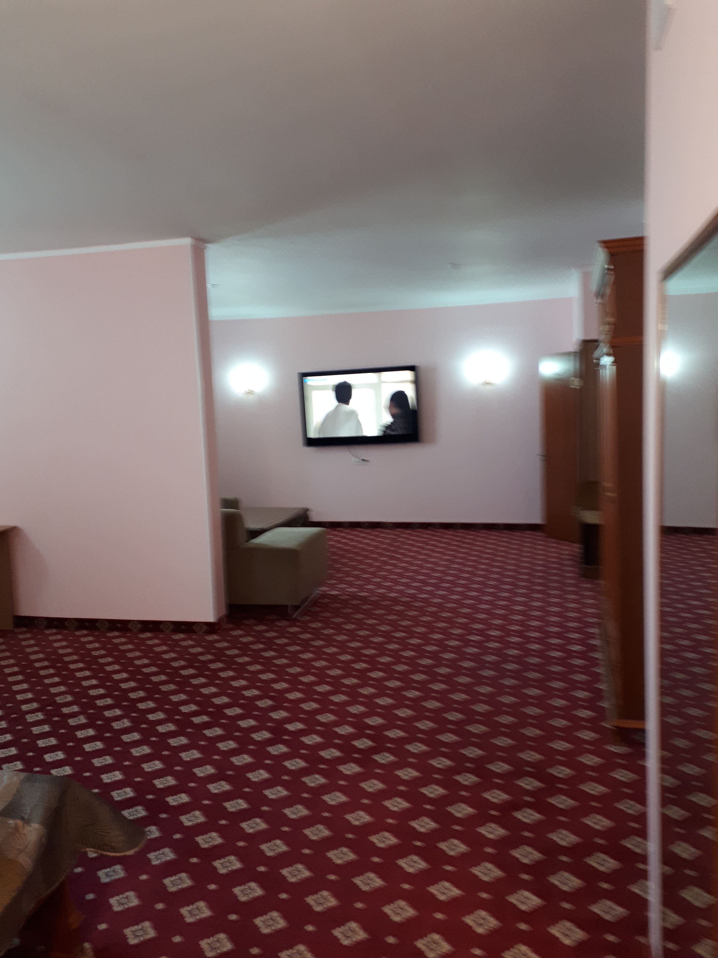 A room with a patterned carpet, a television mounted on the wall, and a sofa.
