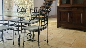 A dining area with a glass table and chairs, a stone wall, a wooden cabinet, and a staircase.