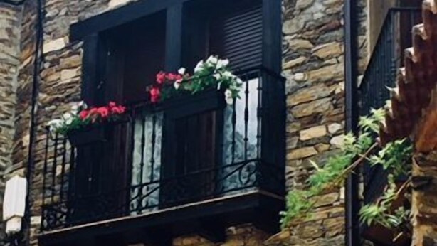 Un edificio de piedra con un balcón decorado con flores rojas.
