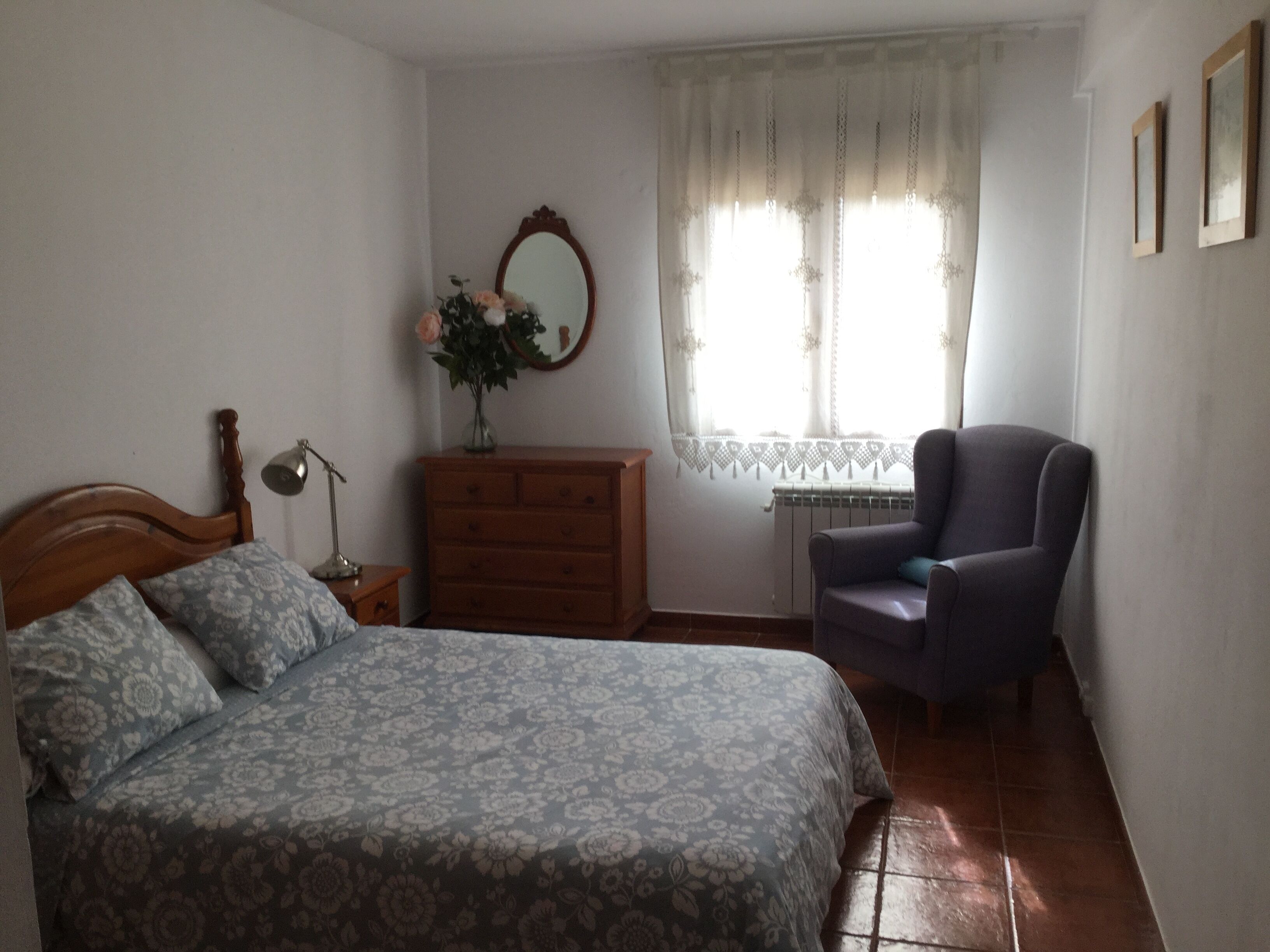 A bedroom with a bed, dresser, chair, and a window with curtains.