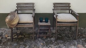 Two wooden chairs with cushions against a wall, a woven basket, and a small table with two cups.