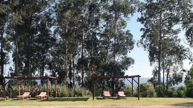 A pool area with two lounge chairs and a pergola with red chairs.