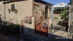 A stone building with a tiled roof, a small balcony with a metal railing, and a white umbrella.