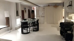 Un vaste espace dédié à la salle à manger, avec une table ronde et des chaises, un mur blanc agrémenté d’un panneau décoratif et un plafond avec des poutres apparentes.