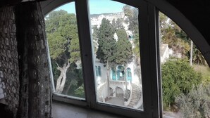 Une vue à travers une fenêtre dont le cadre est incurvé, donnant sur un bâtiment avec un escalier et des arbres.