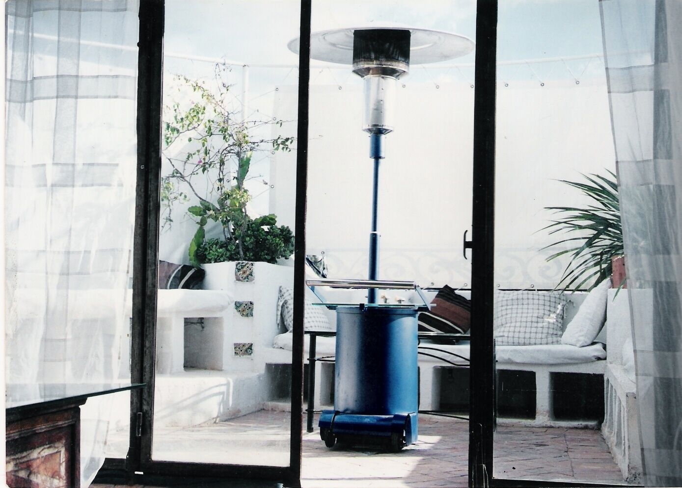 A patio with a blue barrel, a white sofa, and a potted plant.