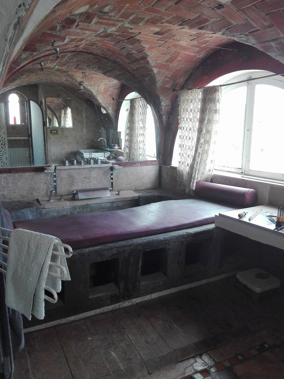 Um quarto com teto de tijolos, janela com cortinas, pia e um banco.