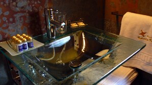 Une salle de bain avec un lavabo en verre, une serviette et des articles de toilette posés sur le comptoir.