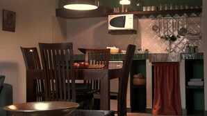 Un coin repas avec des chaises en bois, une table, un saladier, un four à micro-ondes et des ustensiles de cuisine suspendus.