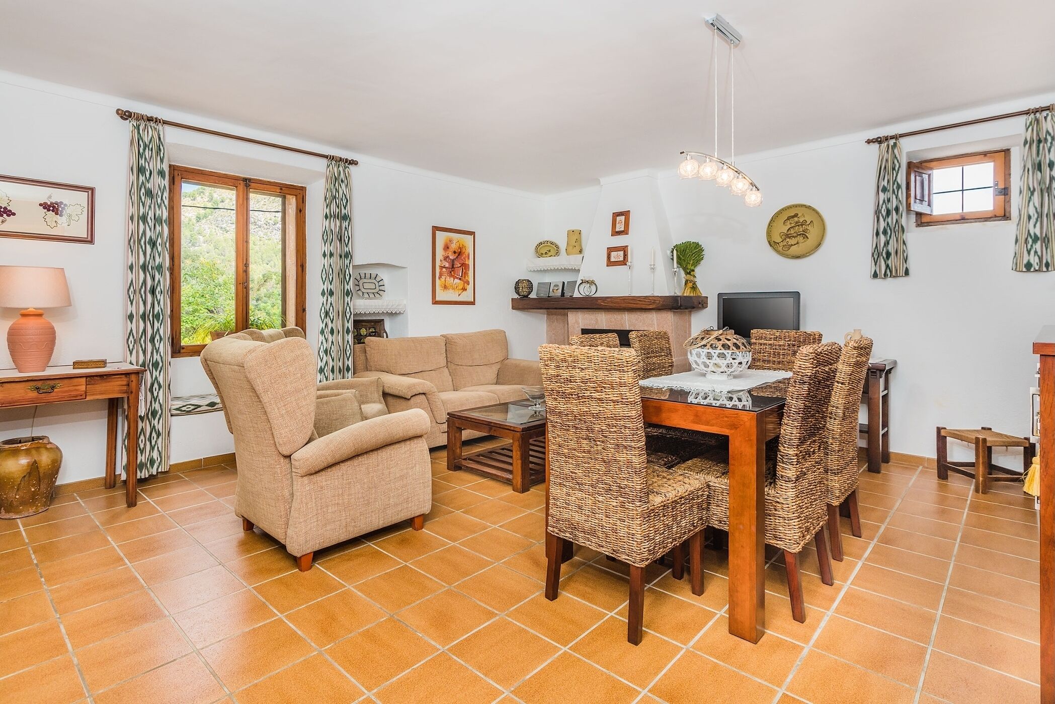 A living room with a sofa, a dining table with wicker chairs, a fireplace, and a television.