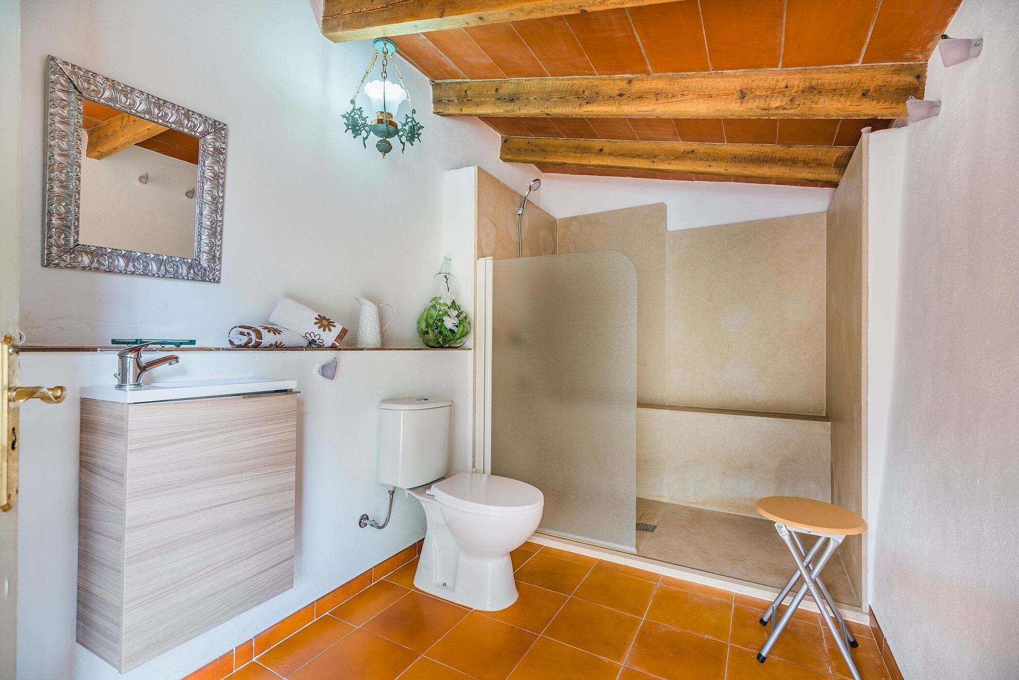 A bathroom with a wooden ceiling, a white sink, a toilet, and a shower enclosure.