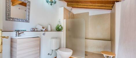 A bathroom with a wooden ceiling, a white sink, a toilet, and a shower enclosure.