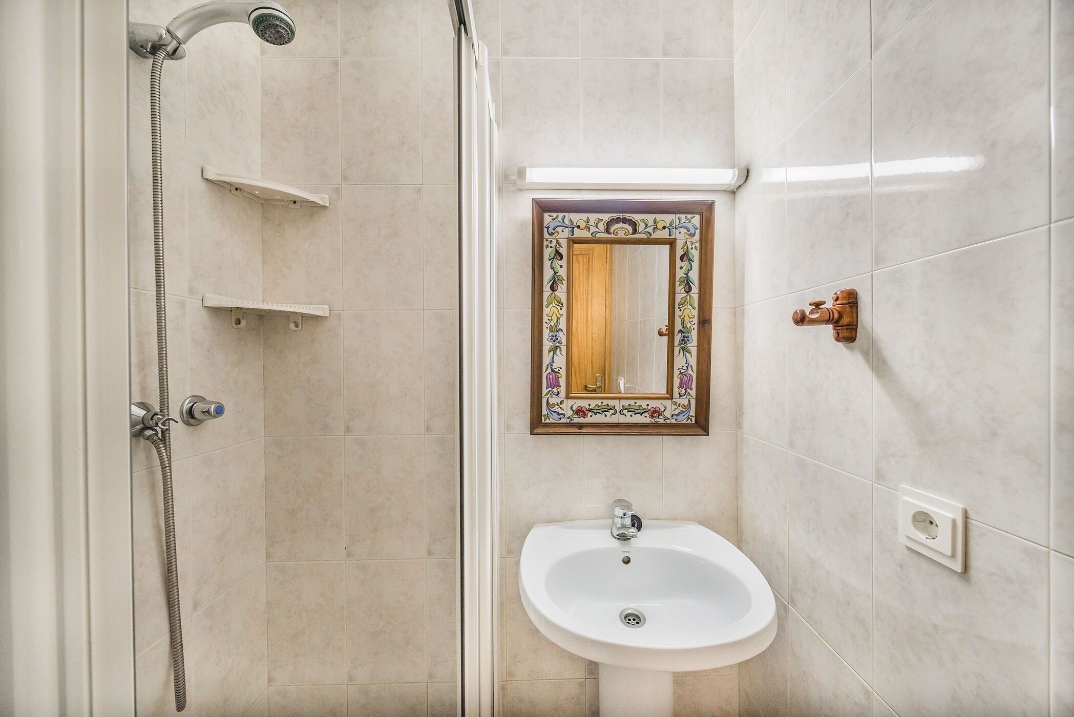 A bathroom with a shower, a sink, and a mirror with a decorative frame.