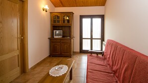 Una stanza con soffitto in legno, un armadio in legno con televisore, un divano rosso e una porta.