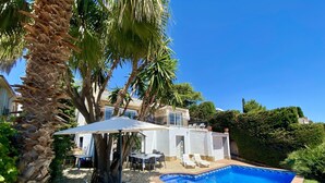 A poolside area with white lounge chairs, a covered patio, and a swimming pool.
