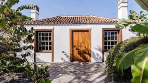 Un bâtiment blanc avec un toit en tuiles, une porte en bois et deux fenêtres avec des volets.