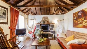 Un salon chaleureux avec une cheminée, des poutres apparentes en bois au plafond, un canapé, un téléviseur et un tableau accroché au mur.
