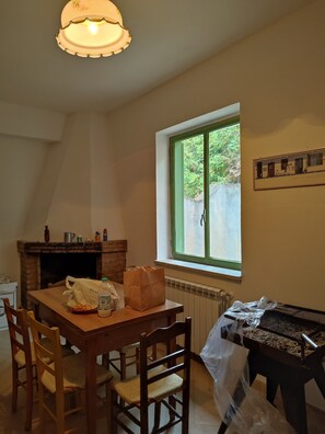 A dining area with a table, chairs, a fireplace, a window with a view, and a grill outside.