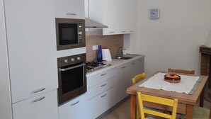 Een compacte keuken met witte kastjes, een magnetron, een oven en een eettafel met stoelen.