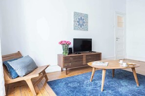 A living room with a wooden bench, a TV on a wooden cabinet, a round coffee table, and a blue rug. - Casa da Avenida IV Lisboa (Lisbon)