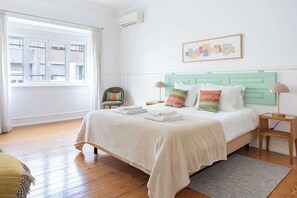 A bedroom with a bed, bedside tables, a chair, a window, and a wall-mounted artwork.