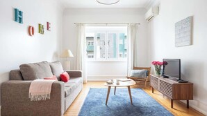 Un salon avec un canapé, une table basse, un meuble pour la télévision et une fenêtre avec des rideaux.
