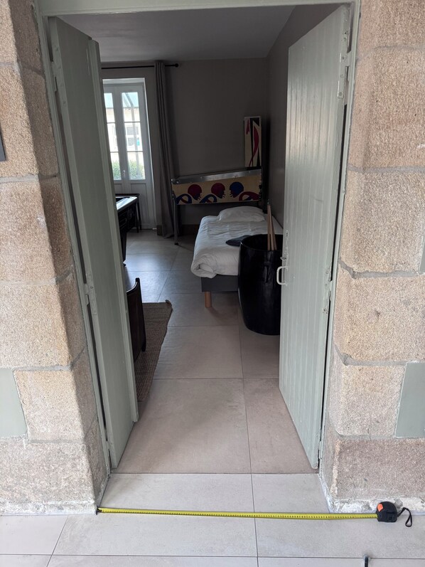 Un couloir étroit mène à une chambre à coucher qui contient un lit, une table de chevet et une fenêtre.