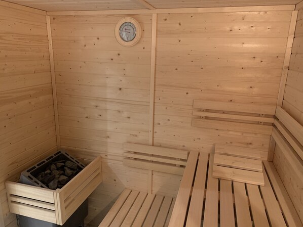 A wooden sauna with benches and a wall-mounted thermometer.