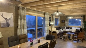 Ein gemütliches Blockhauss-Interieur mit Essbereich, einer Couch und einem großen Fenster mit Blick auf eine Terrasse.