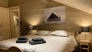 Ein schlafzimmer mit Holzwänden, einem Bett, zwei Nachttischlampen, einem Gemälde von einem verschneiten Berg und einem Nachttisch mit Lampe.