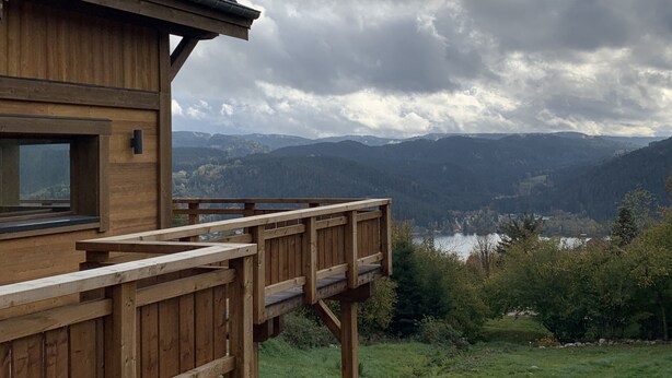 Eine Holzhütte mit einer Terrasse mit Blick auf einen See und Berge.