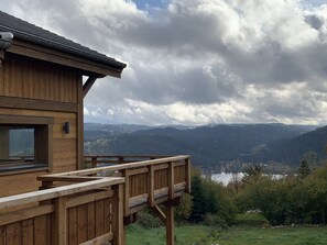 A wooden cabin with a deck overlooking a lake and mountains.