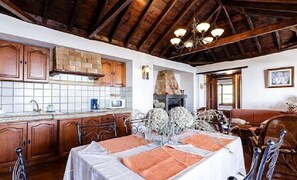 A rustic kitchen with wooden cabinets, a stone fireplace, and a dining area with a table set for two.