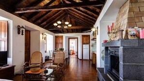 A cozy living room with a fireplace, wooden beams, and a dining area with chairs and a table.