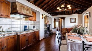 A rustic kitchen with wooden cabinets, a tiled backsplash, and a stone fireplace.