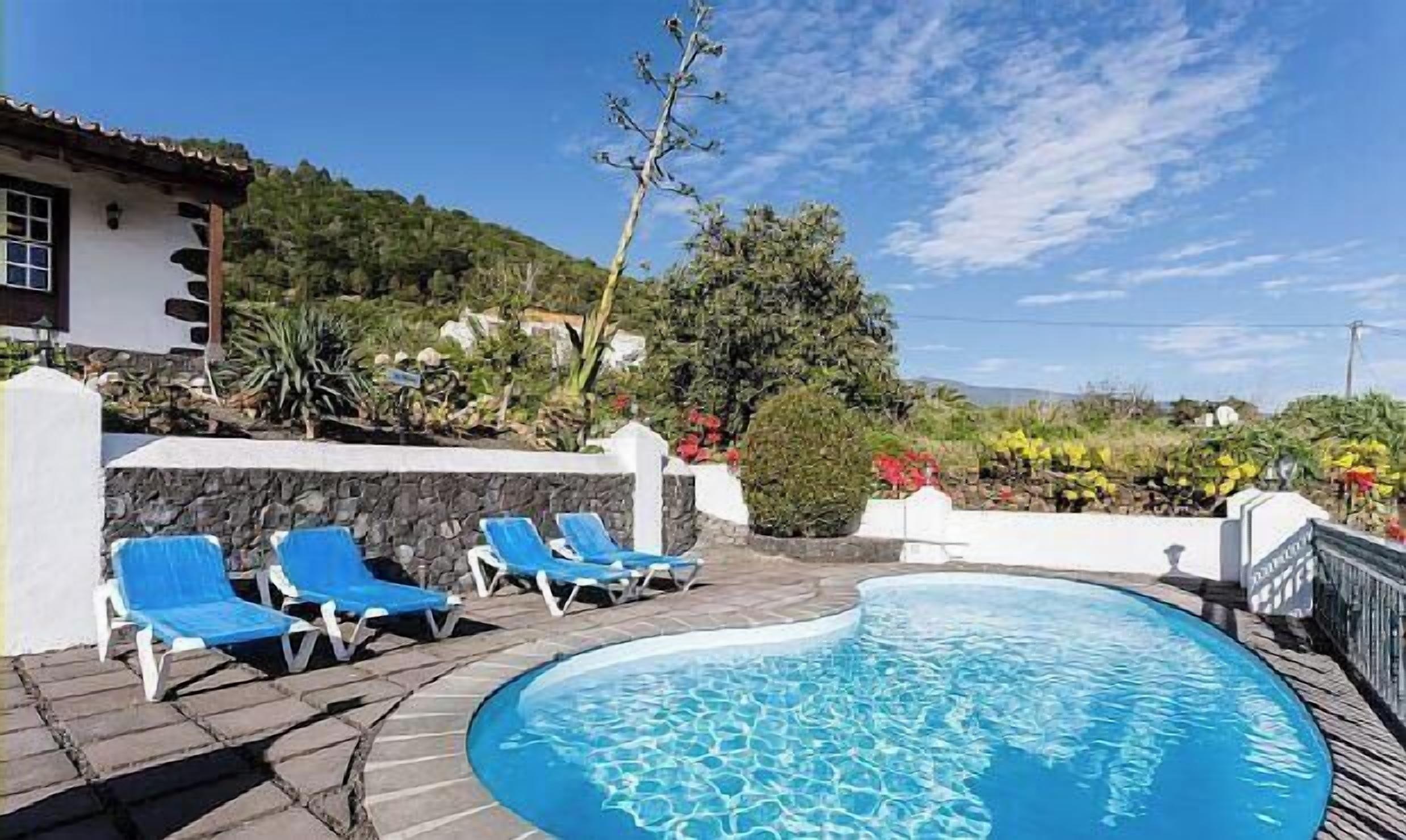 A pool area with blue lounge chairs, a stone wall, and a view of the surrounding landscape.