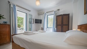 Een net opgemaakt bed met witte lakens, een houten hoofdbord en een aan de muur bevestigde televisie.
