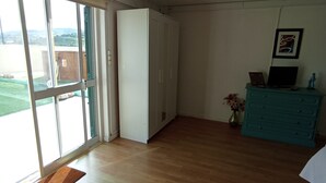 A room with a large sliding glass door leading to a balcony, a white wardrobe, a teal dresser, and a framed picture on the wall.