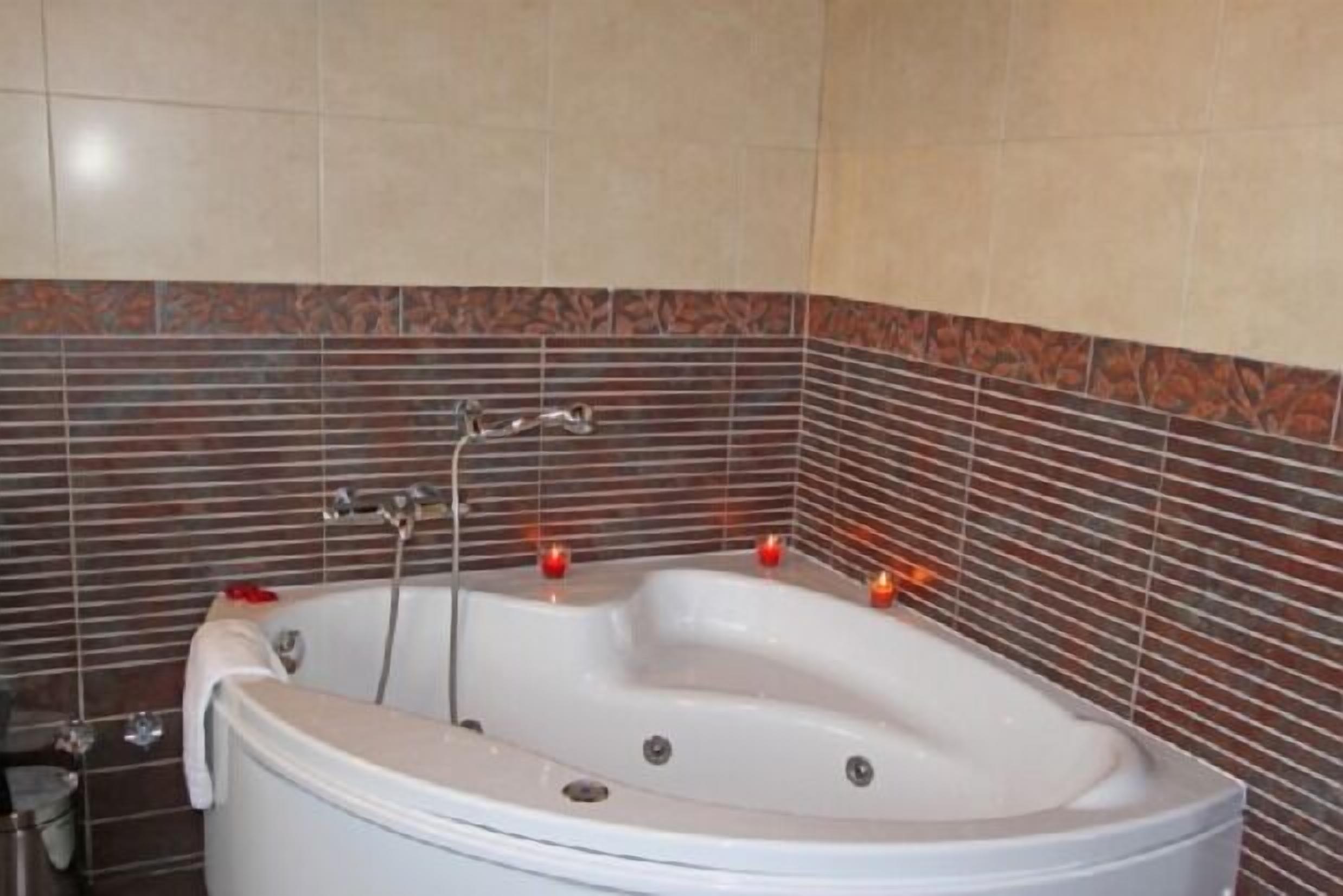 Eine weiße Badewanne mit Duschkopf, vor einer mit Blattmuster gefliesten Wand.